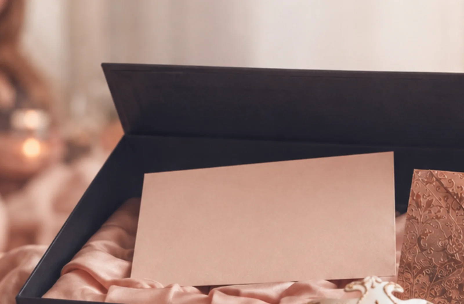Geöffnete schwarze Box mit rosé Seidenfutter, Karte und kupferfarbenem Umschlag